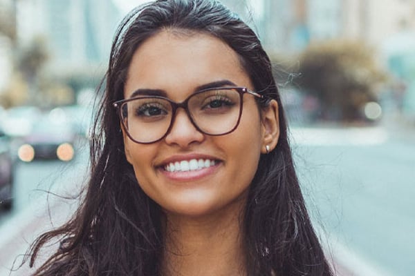 Woman wearing glasses smiling at camera with urban street background