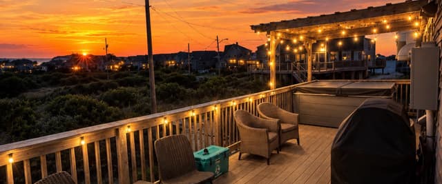 Elevated deck with lounge chairs and string lights overlooking sunset, coastal homes, and marshland at dusk